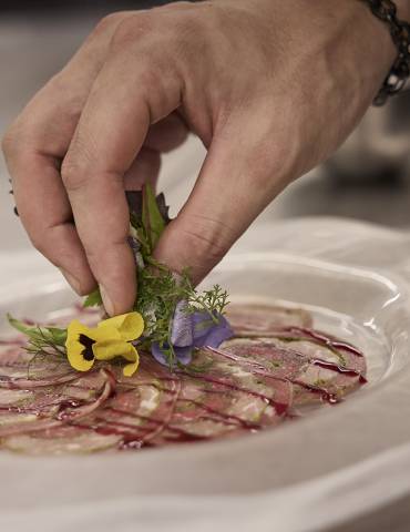 Chef prepares carpaccio with herbs and flowers